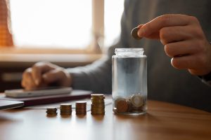 Stacks of coins and a man dropping a coin into a jar.